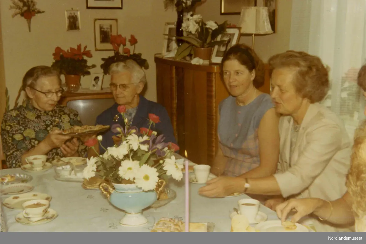 Kvinner sitter rundt et bord. Kaffekopper og søtbakst. I bakgrunnen sees et fjernsynsapparat, planter og bilder. Nr. 2 fra venstre er Klara Simonsen. Nr. 3 fra venstre er Ellinor Simonsen.