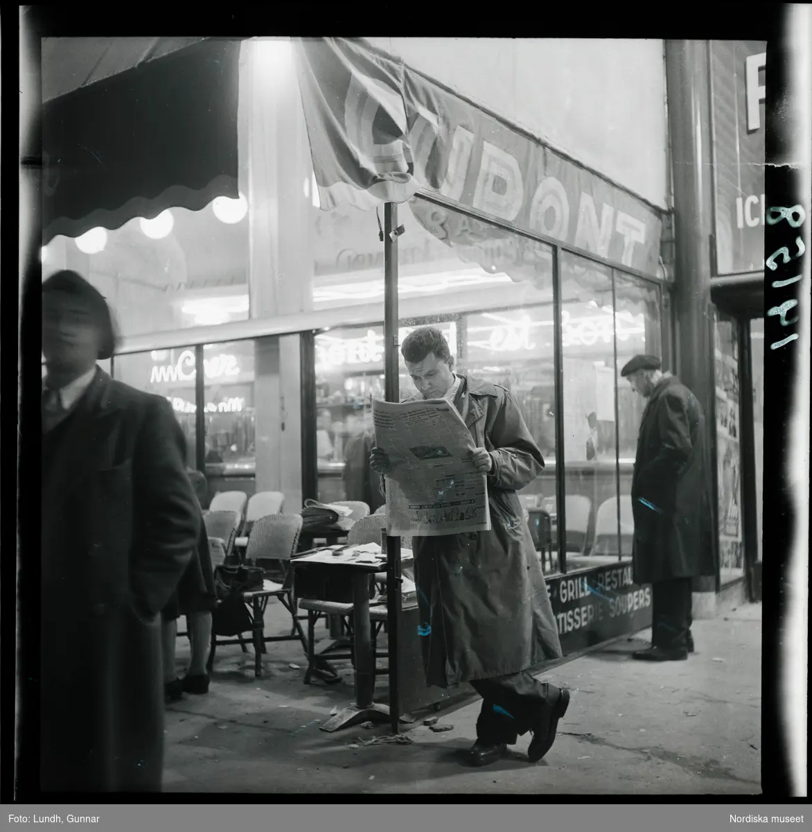 1950. Paris. Man står och läser tidning vid en bar