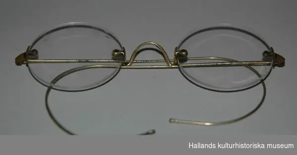 a) Glasögonen har infattade glas och skalmar av mässing. b) Fordral av papp.