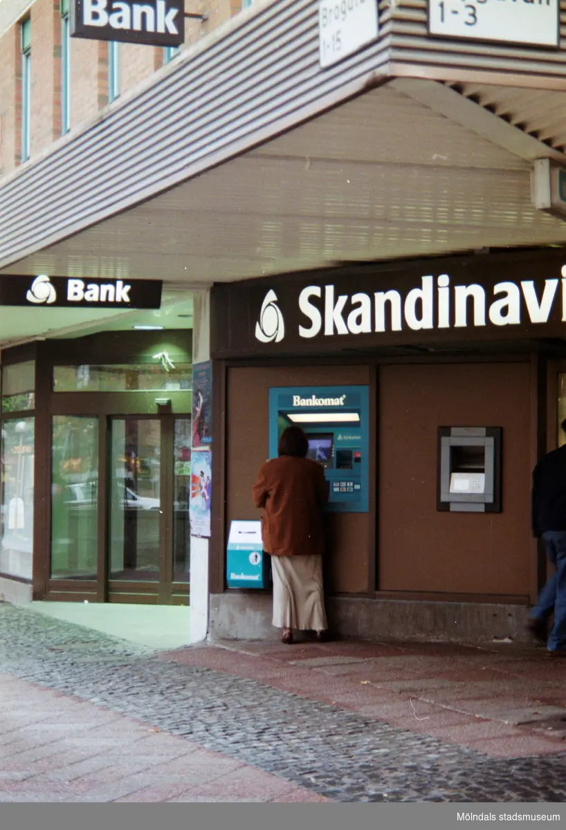 Skandinaviska Enskilda Banken och en Bankomat i hörnet av Brogatan/Nygatan. Mölndalsbro i dag - ett skolpedagogiskt dokumentationsprojekt på Mölndals museum under oktober 1996. 1996_1190-1211 är gjorda av högstadieelever från Kvarnbyskolan 9D, grupp 4. Se även 1996_0913-0940.