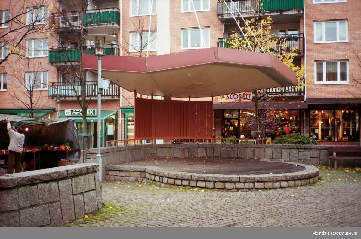 Torghandel och en scen på Alberts torg. Mölndalsbro i dag - ett skolpedagogiskt dokumentationsprojekt på Mölndals museum under oktober 1996. 1996_1227-1245 är gjorda av högstadieelever från Kvarnbyskolan 9D, grupp 6. Se även 1996_0913-0940.