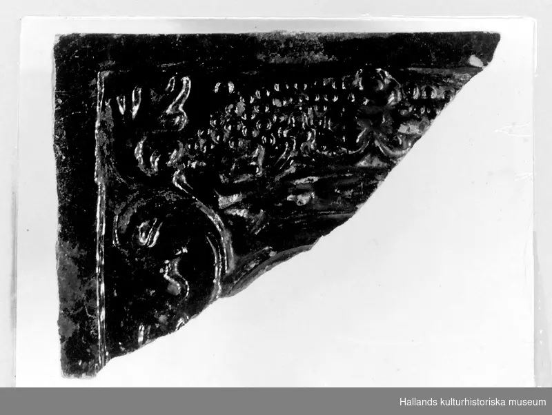 Arkeologiskt föremål. Fragment av kakel. Hörn. 
Svartglaserat. Dekorerat, växtrankor med kunglig krona.