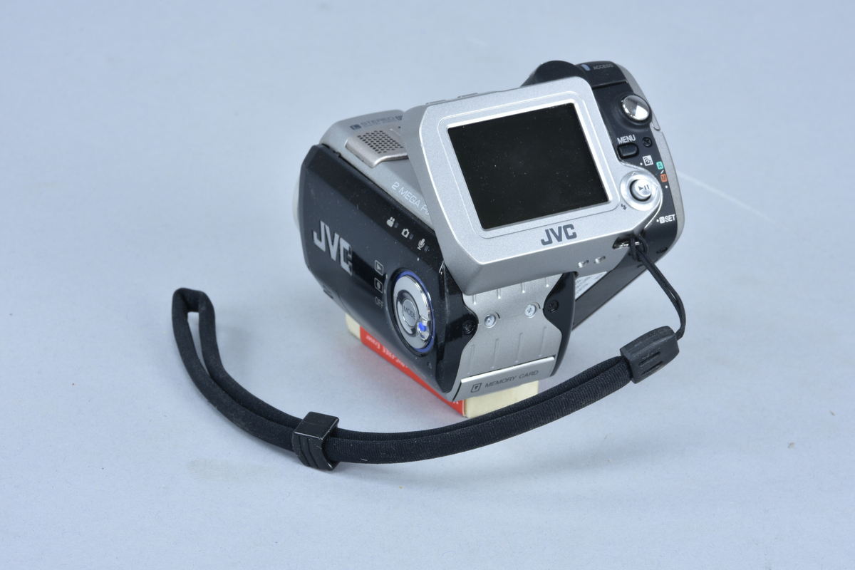 Digital mediakamera 2 megapixlar med inbyggd stereomikrofon JVC typ GZ-MC200E nr 00000001 (förserieexemplar). För lagring på minneskort typ Microdrive. Zoom 1:1.8 brännvidd 4.5-45 mm med autofokus, 10x "optical zoom". Vridbar så att displayen på baksidan är lätt att se. Plats för Microdrive med Compact Flash II -anslutning samt batteri.
