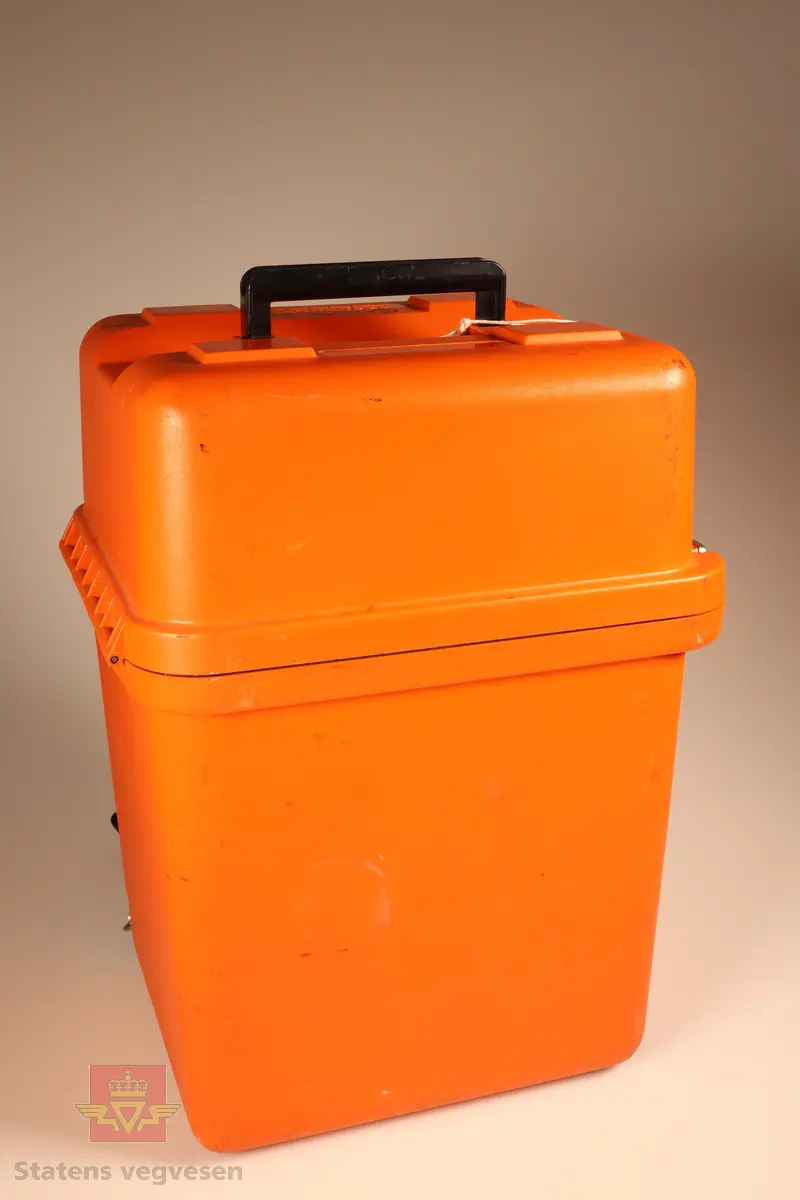 Grønn og svart elektronisk teodolitt med oransje koffert. I kofferten er det en elektronisk teodolitt oppå en GDF22 Fotplate, et ekstra batteri, en skrutrekker, regntrekk, instruksjonsmanualer, reservedeler og en mini prismestang med libelle.