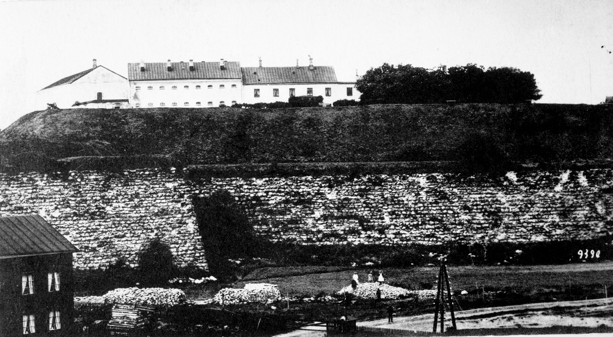 Kolorerat vykort. Utsikt mot fästningen med vallgraven i förgrunden. T v uppe på fästningsvallen står den sista kanonen på fästningen. Den flyttades till Påskberget 1898.
(Bild 2: motivet i sv/v)