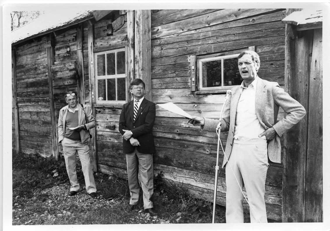 Tre män står utmed ladugården Rasten i Röttle. De är museichefen Olof Fong, museistyrelsens ordförande samt Rolf von Otter som talar i en mikrofon på stativ.