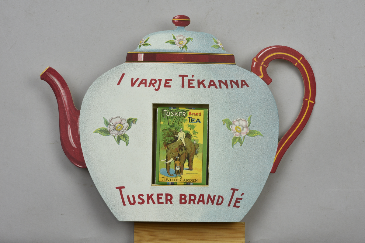 Reklamskylt visande tekanna med ett tepaket. Text: "I varje Tékanna" samt "Tusker brand Té". Paketet separat fotograferat.
