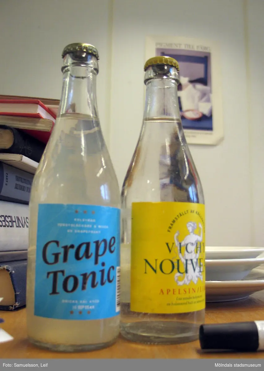 Två dricksflaskor på ett bord. Den ena Grape Tonic, den andra Vichy Nouveau. Interiörfotografi från byggnad vid Soabs industrianläggning i Mölndals Kvarnby, år 2007. Anläggningen användes vid fototillfället av Hexion Speciality Chemicals Sweden AB.