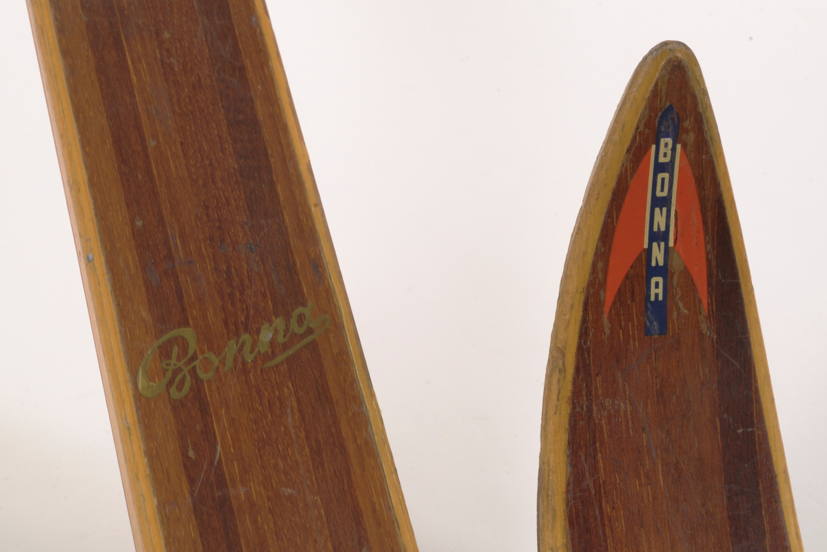 En av et par brune treski (den andre A.06019-01.a) med lysere brune kanter. Laminert tre. Merke på oversiden av skituppen "Bonna" vertikal skrift på blå bakgrunn, røde spisse vinger på hver side av teksten. Rødlakkert Rottefella tåbinding.