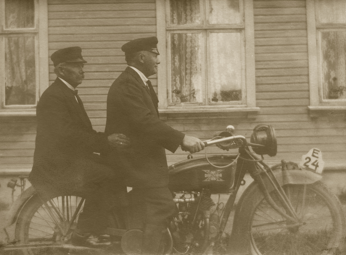 To menn som er ute og kjører på motorsykkel. Det er en engelsk produsert sykkel av type Excelsior Autocycle med registreingsnummer E24