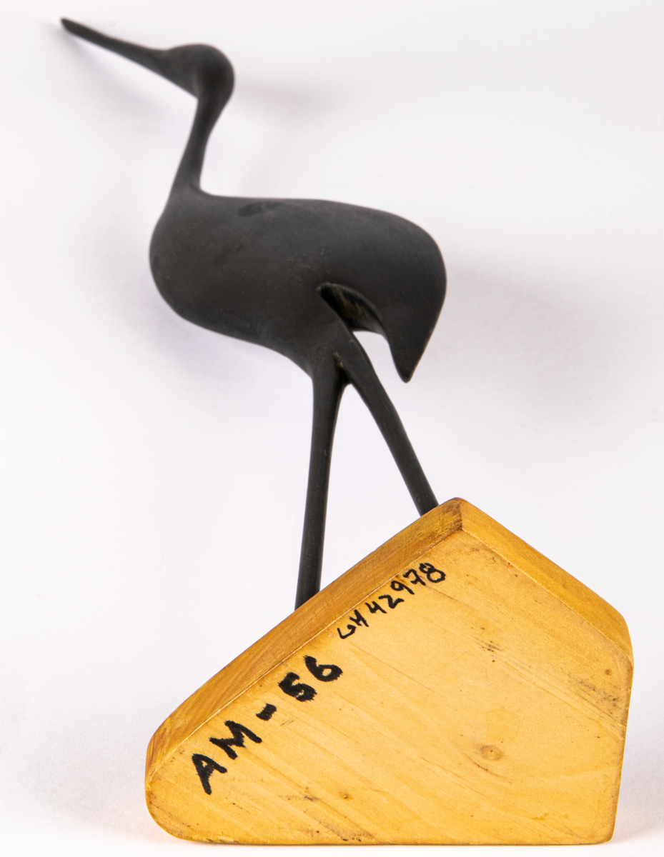 Prydnadsfågel, TV-trana, snidad i trä. Svart fågel, hög och smal, på fot av trä. Märkt i botten "A M - 56".
Vanlig från 1950-talet som prydnadsfigur i hemmen.