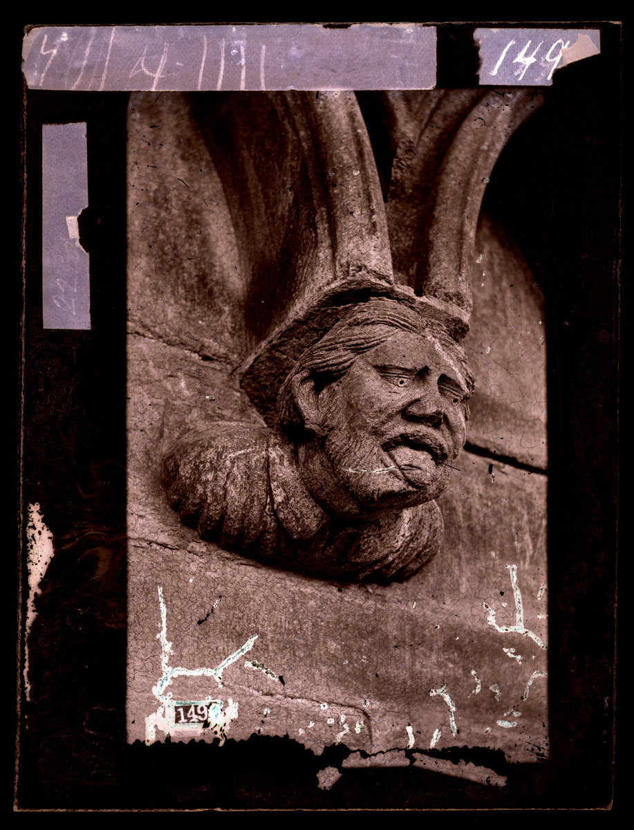 Konsollfigur fra buefrisgesims på nord-østre side av oktogonen i Nidarosdomen. Person som rekker tunge. Bilde tatt før restaurering på 1870-tallet.