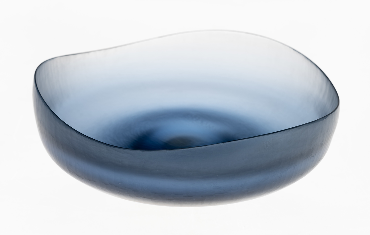 Lav, halvkuleformet skål i farget glass, hvor yttersiden er mattslipt. Bølgende formet munningsrand. Fargen graderes fra mørk ved bunnen, til lys blå på skålens øvre del.