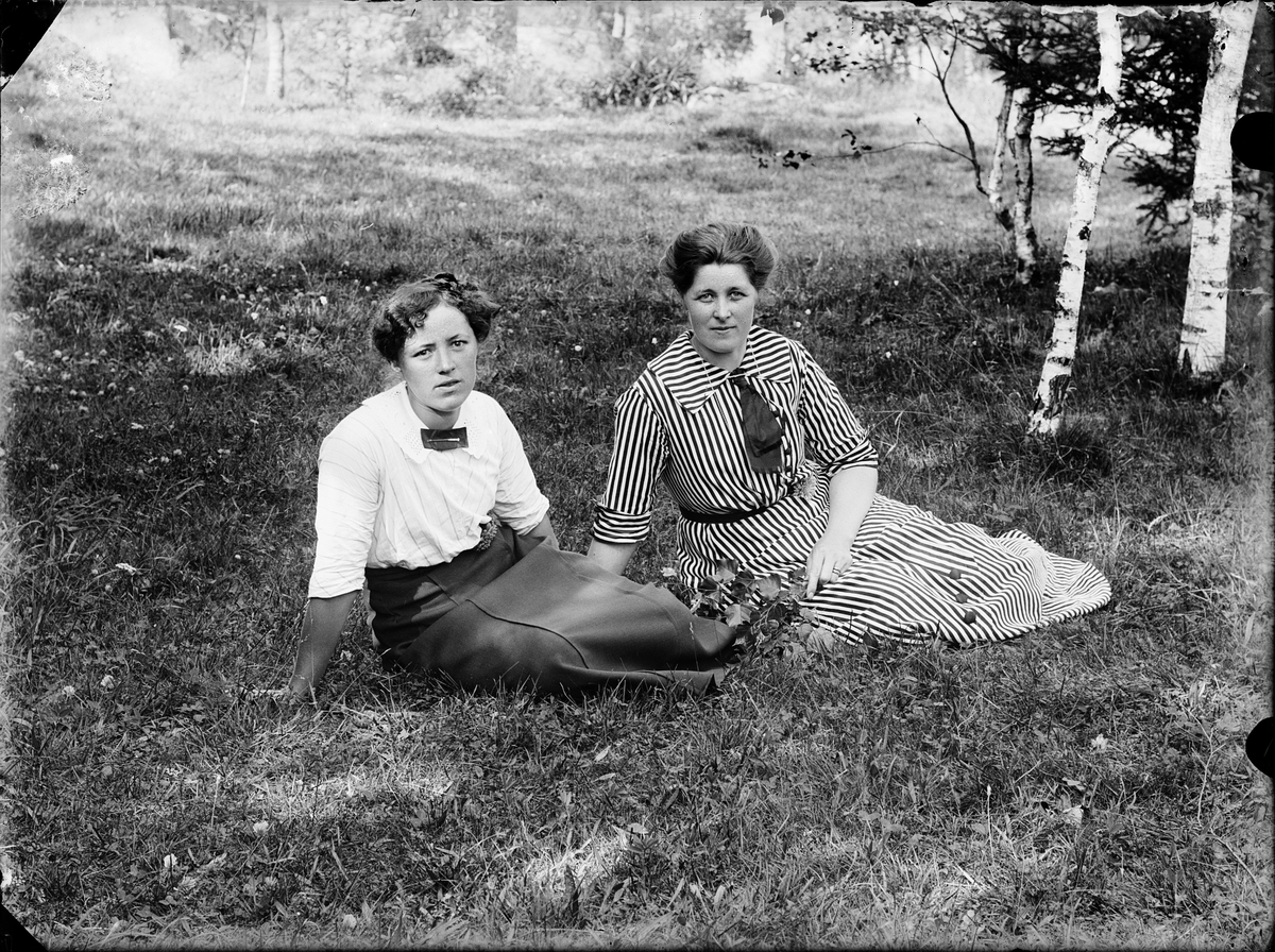 Två kvinnor sitter på gräsmattan i trädgård, Alunda, Uppland