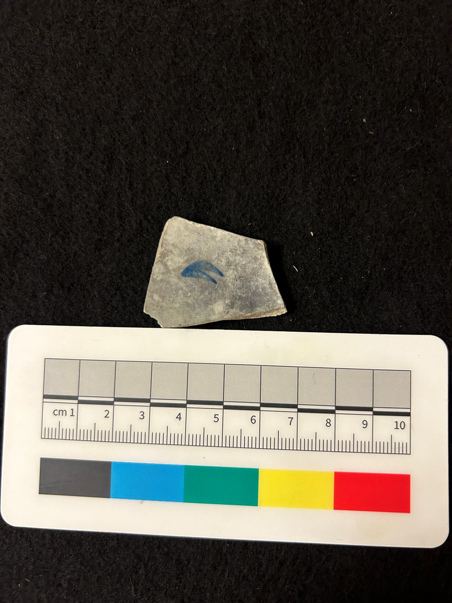 Ett delvis spjälkat fragment flintgods med blå dekor på insidan i form av två "vingar".