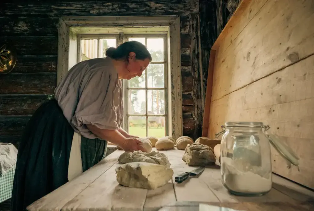 Kvinne i klær fra 1800-tallet baker brød i Nystu på Glomdalsmuseet