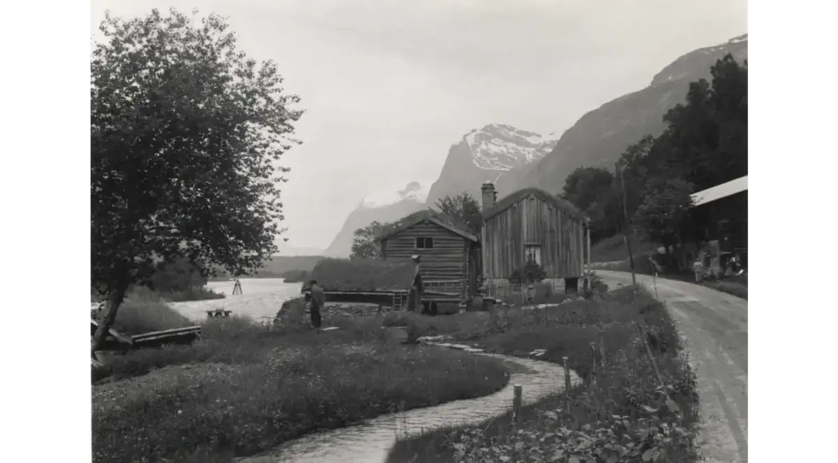 Gårdstun ved elva Driva med fjell i bakgrunnen, en vei går gjennom tunet.