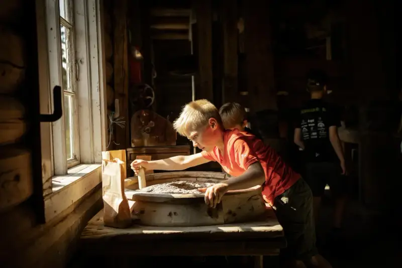 Barn prøver ut håndkverna på Eggedal Mølle, tungt arbeid for en liten kropp.