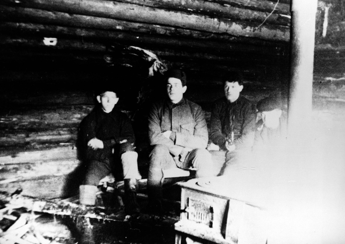 Fire menn ved ovnen inne i koie ved søndre Kyltjern i Losby.
