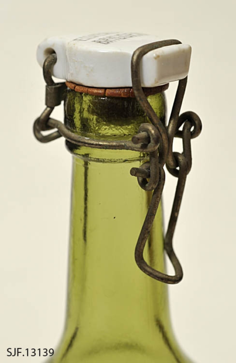 Flaske av grønt glass, antakelig opprinnelig brus- eller ølflaske, som kan ha vært gjenbrukt til aldre drikkevarer, for eksempel husholdningssaft. Flaska er 20,0 centimeter høy (uten kork). Den har en sylindrisk kropp med cirka 7,0 centimeters diameter. Cirka 10 centimeter fra standflata går den sylindriske delen over i ei innoverskrånende skulder mot en mer sylindrisk hals. Den midtre delen av flaskebotnen er oppoverkuvet. Flaska kan romme cirka 3 desiliter væske. Godset omkring munningen - «flasketuten» - er noe tjukkere enn i flaska for øvrig, og her er det et spor som har gitt feste for en såkalt «patentkork». Dette er en propp, utført i kvitt porselen, som er hengslet til flasketuten ved hjelp av ståltråd, som er forankret i det nevnte sporet omkring flasketuten slik at proppen faller ned i flaskemunningen og kan låses der ved hjelp av ei ståltrådspenne, som når flaska lukkes omslutter en tapp i den fremre enden av porselenselementet. Undersida av denne komponenten har vært utstyrt med en rødfarget gummipakning, som skulle skape et vakuum i flaska. Her er pakningen bare delvis intakt. Oversida av porselenselementet er merket «ELVERUM BRYGGERI» (jfr. fotografiet SJF-F.013394).