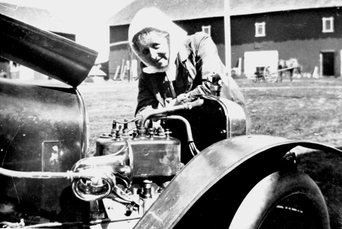 Thora Løken ved en Adler bil modell 1914, D-53. Hun var første kvinne som tok førerkort i Hedmark i 1914. Her på gardstunet på Granerud gård, Brumunddal.