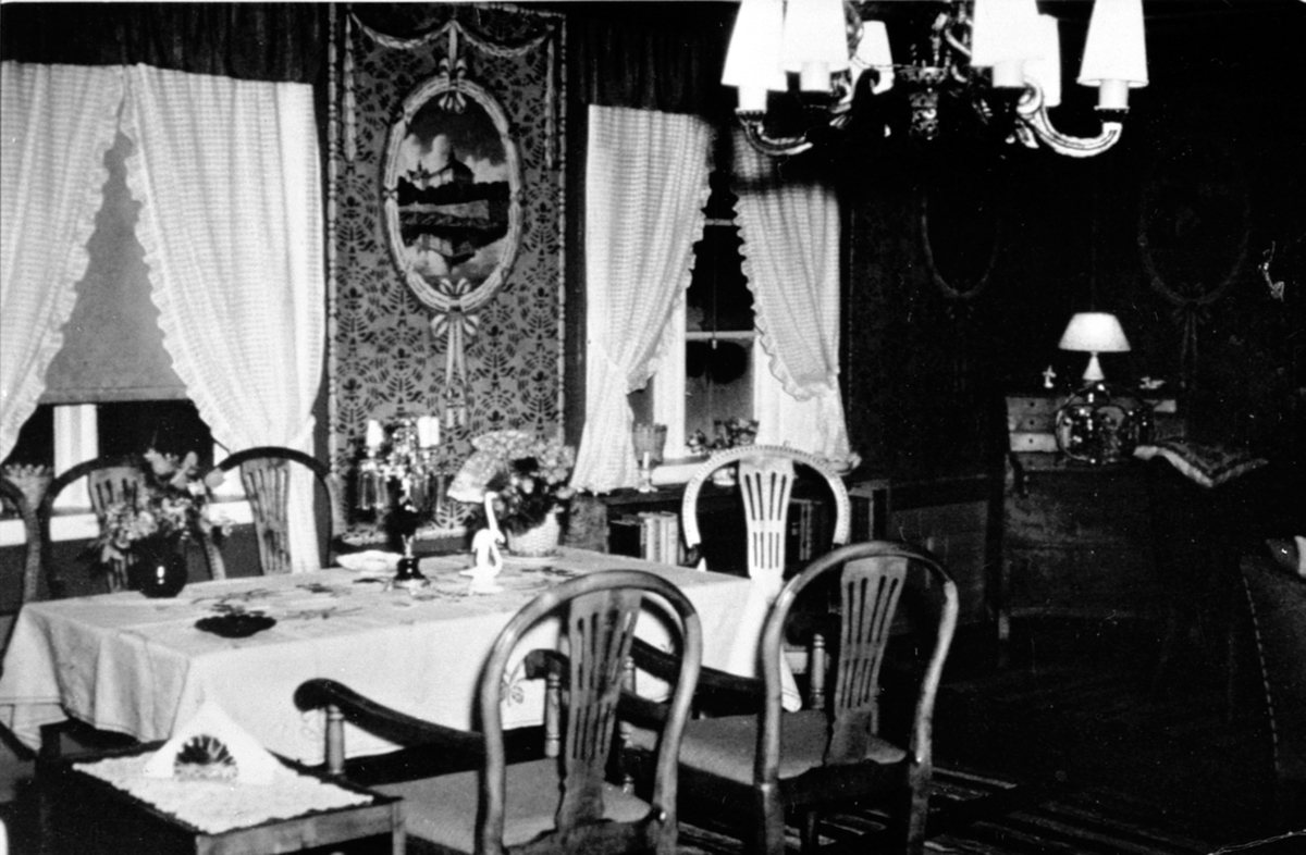 Interiør, stue, veggdekor malt på papp av Rudolf Krogh, spisestue med pyntet bord, skatoll, stoler, lampe, gardiner, Bogsti gård, Veldre, Ringsaker.