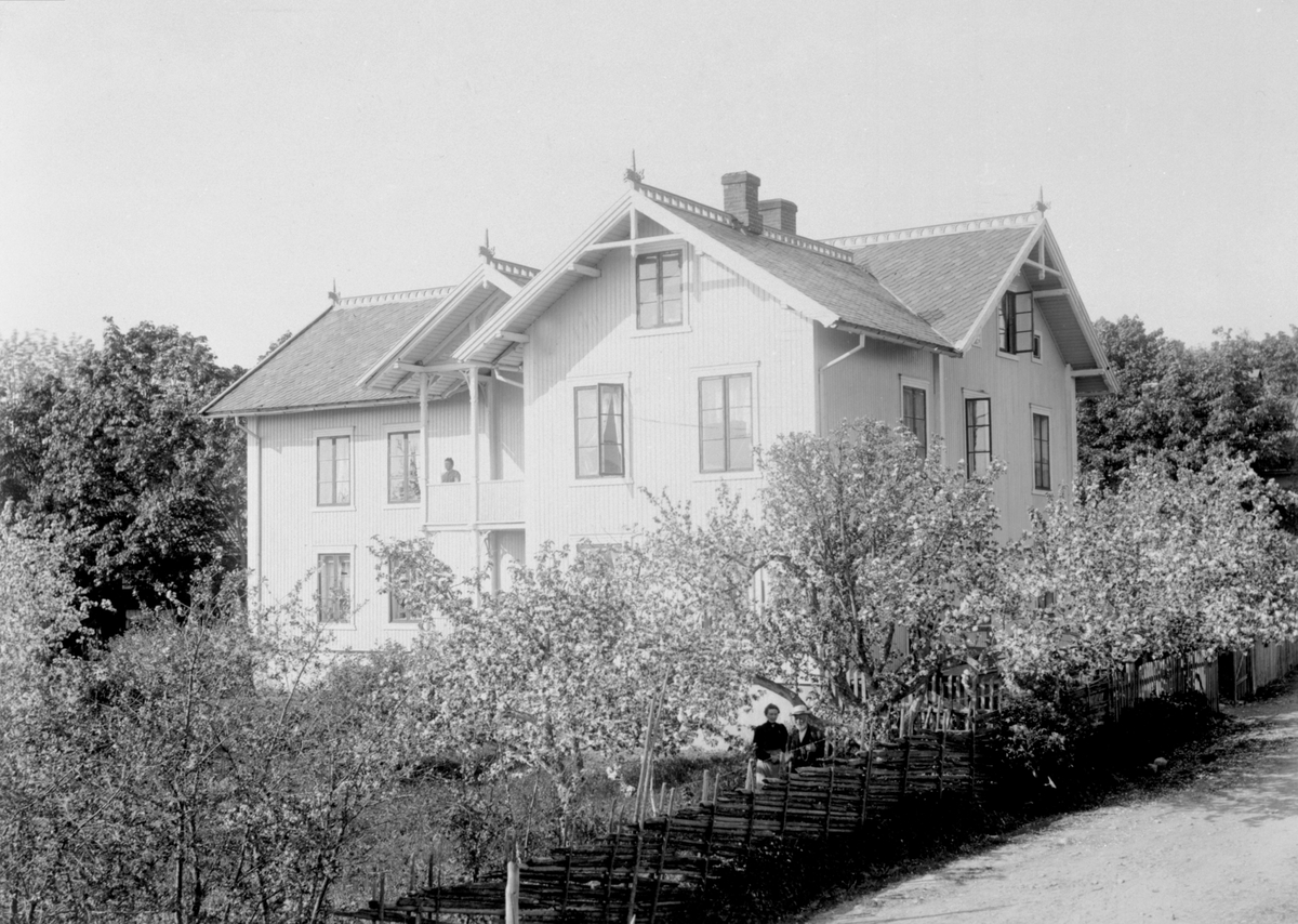 Eksteriør hovedbygningen på Helgeby, Nes, Hedmark. Syverine Helgeby (1866-1923) på veranda. Anna Lie (1869-1934) og Jacob Lie (1832-1918) i hagen ved skigard.