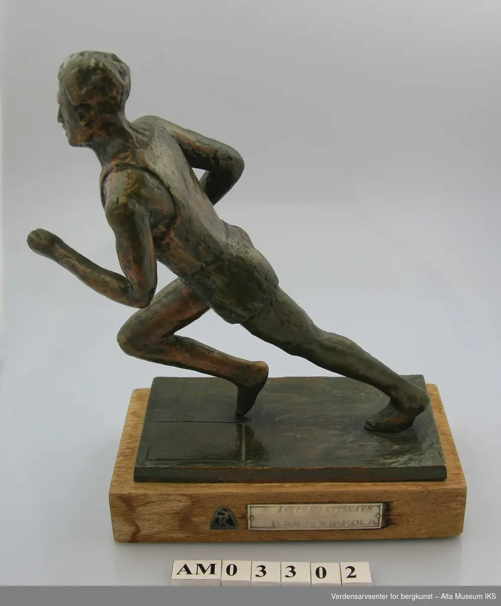 Form: Løpende atlet i bronse, montert på trebase med emblem
