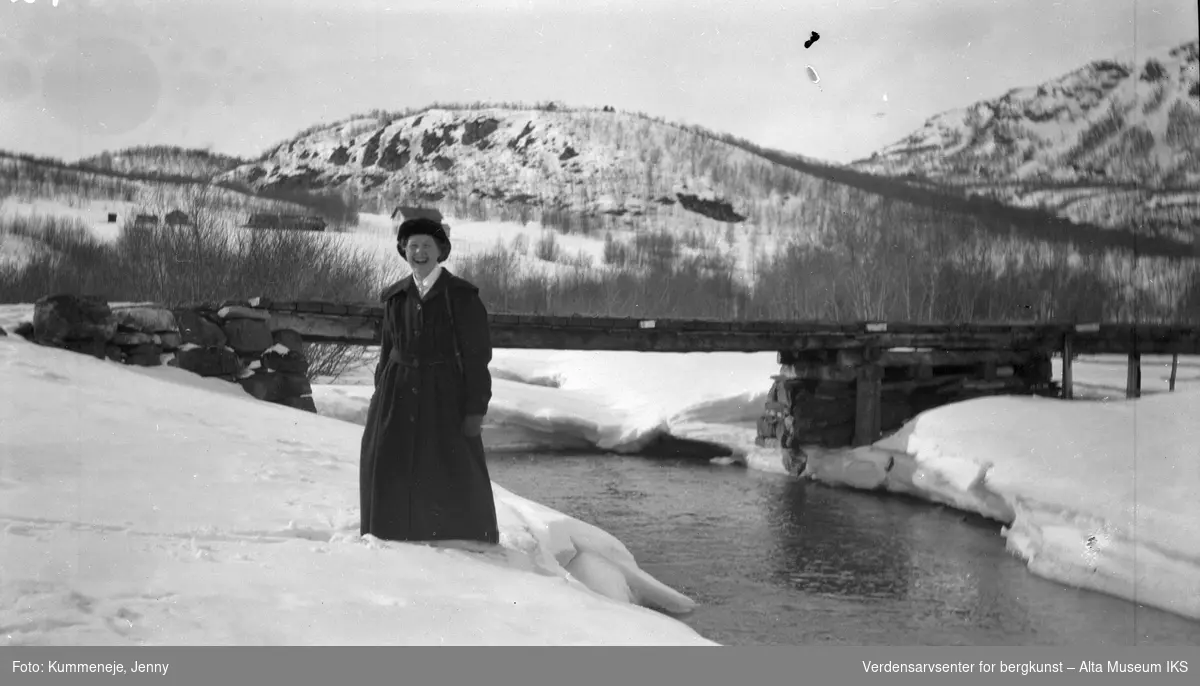 Kvinne ved storelva med vinter landskap i bakgrunn. 1919.
