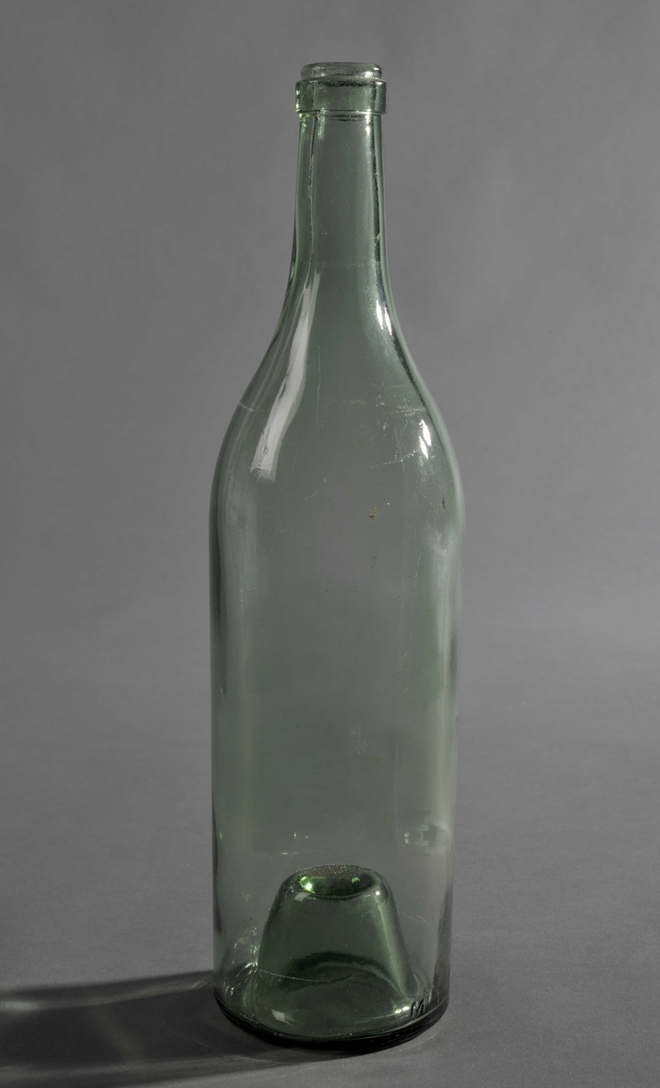 Blank med grønt skjær, støpt glassflaske med konkav bunn. Bunnkjeglen er ganske markant. Flasken smalner til munning ved 2/3 høyde.