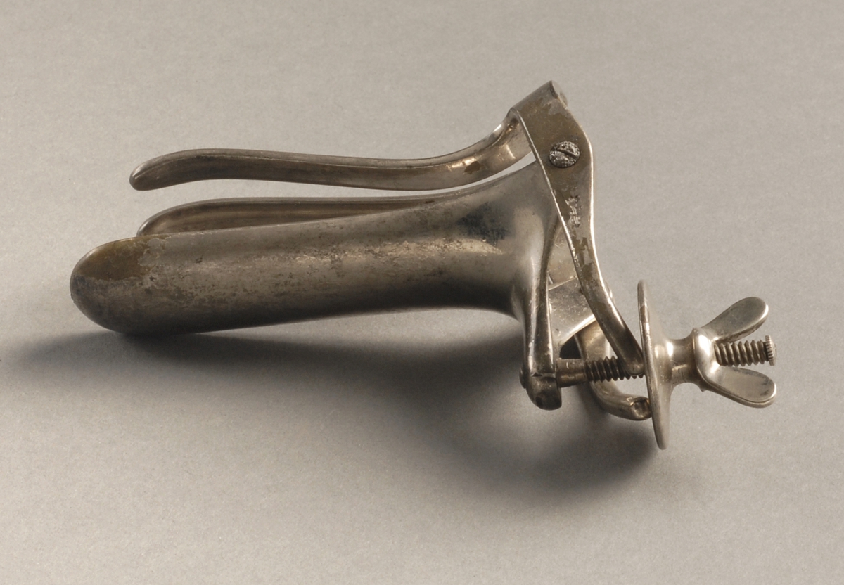 Metallinstrument med vingeskrue, ene enden er andenebbformet, nebbet kan åpnes, i andre enden er det en konstant sirkulær åpning.
