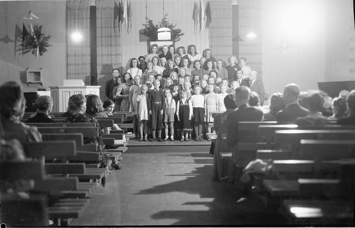 BARNESANGKOR I BEDEHUSET I MOELV. Søndagsskolestevne fra 1944-45 på Moelven bedehus (Kjærstad elektriske). Noen av de voksne: Ole Hagen til venstre i koret, John Strømman og pastor Kr Syvertsen til høyre. 