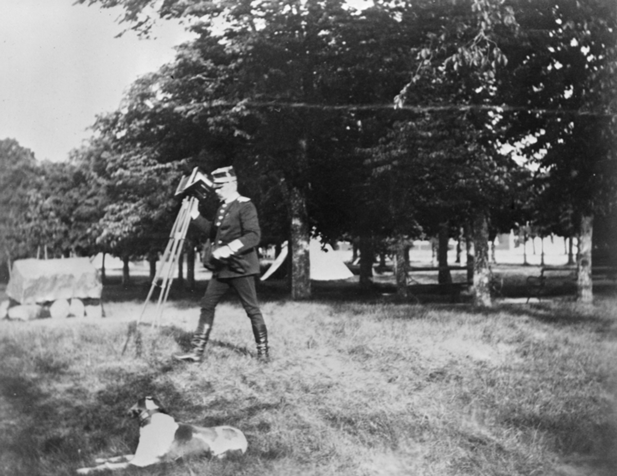 General Lovén, chef för Andra livgrenadjärregementet bär på en kamera. En hund ligger bredvid i gräset.