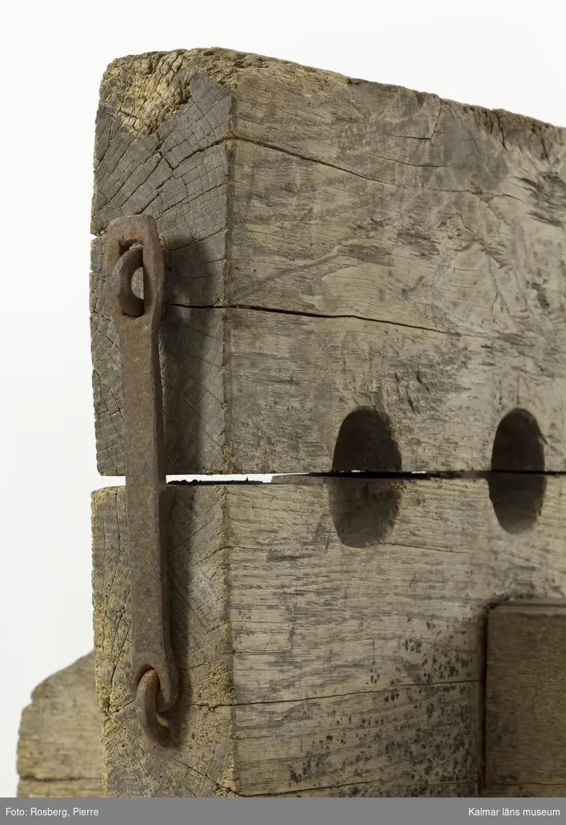 KLM 9392. Straffstock. Av trä med järnbeslag. Straffstocken består av fyra delar, sammanfogade med kilar och stora järnspikar. En sittbräda och en kluven planka med åtta hål där benen låstes fast. Tjärad. Träet är sprucket på olika ställen.
