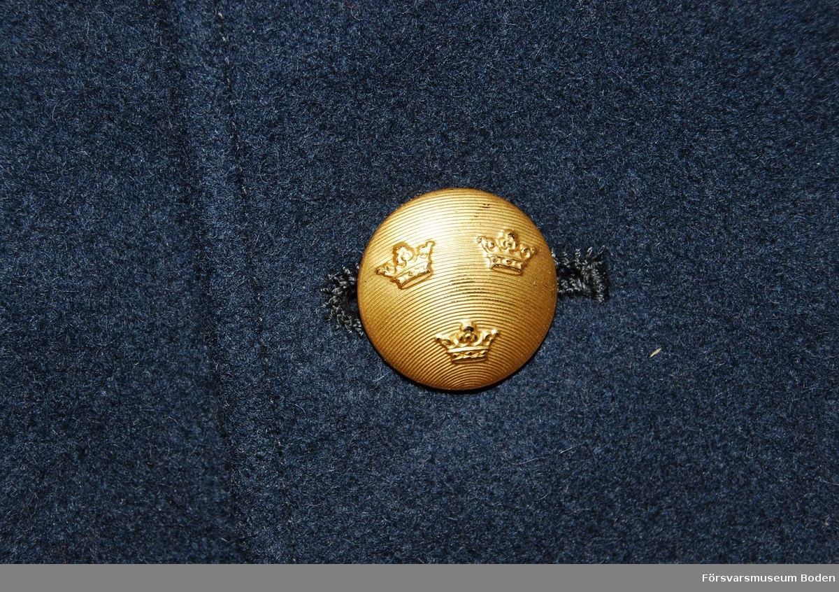 Stålgrått kommisskläde. Dubbelknäppt med tre rader guldfärgade knappar med tre kronor. Hemvärnstecken m/1946-1960 på kragspeglarna, samt tillsammans med två stjärnknappar m/1960 på axelklaffarna. 