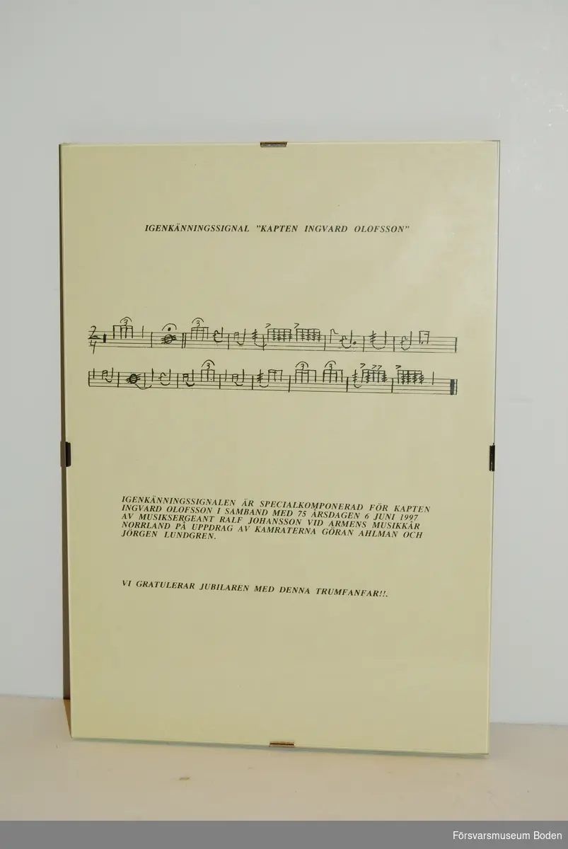 Glasad tavla med noter till igenkänningsignal för kapten Ingvard Olofsson i samband med dennes 75-årsdag 6 juni 1997. Signalen är komponerad av musiksergeant Ralf Johansson vid Arméns musikkår Norrland.