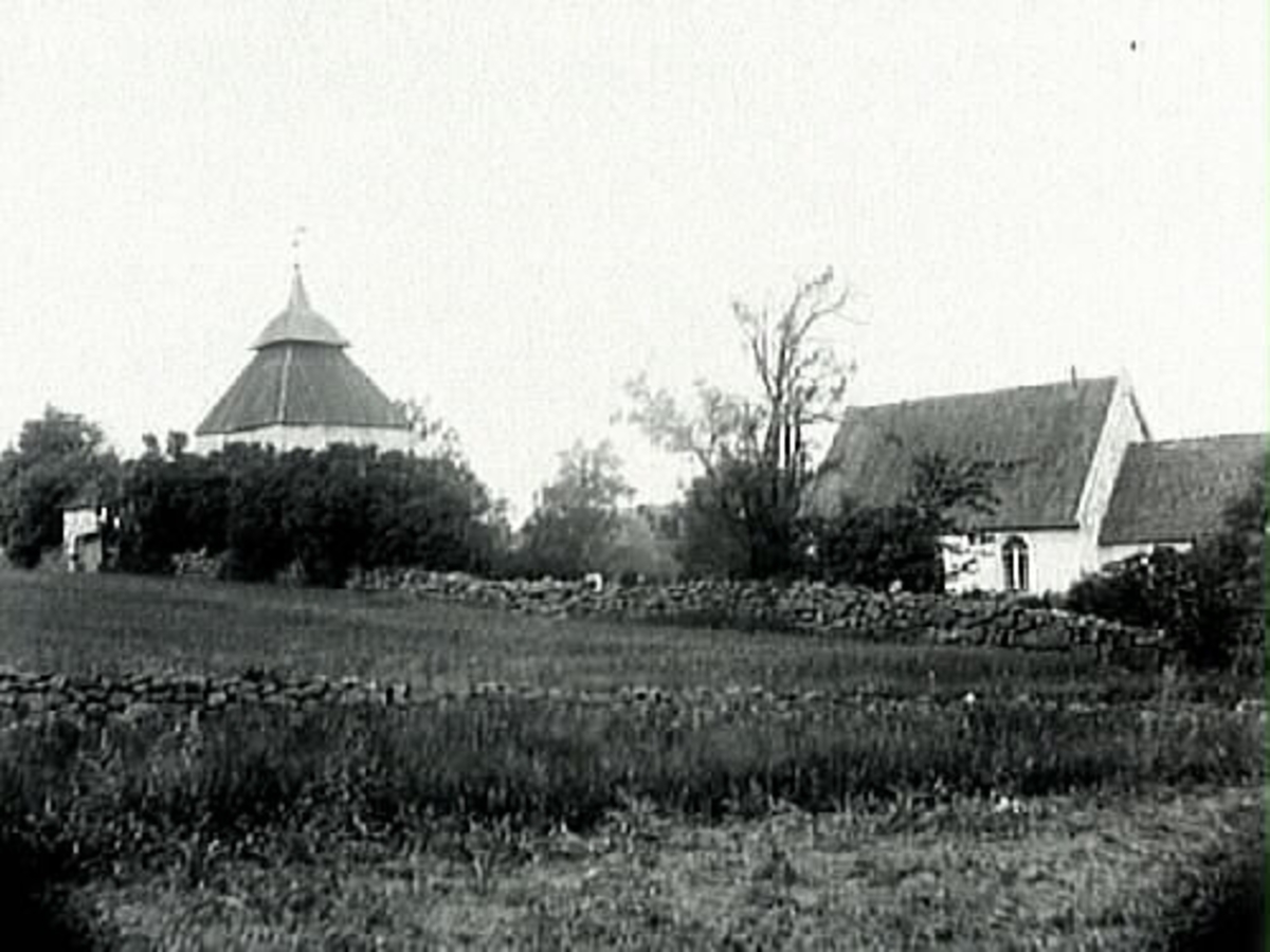 Köinge gamla kyrka med klockstapel och stiglucka. I förgrunden fält med stenmurar.