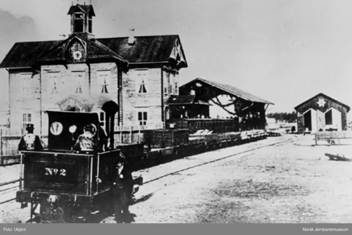 Damplokomotiv type I nr. 2 med stasjonsbygningen, toghallen og lokomotivstallen i bakgrunnen
