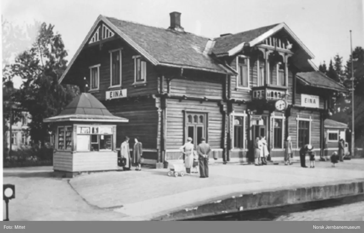 Eina stasjonsbygning med reisende på plattformen