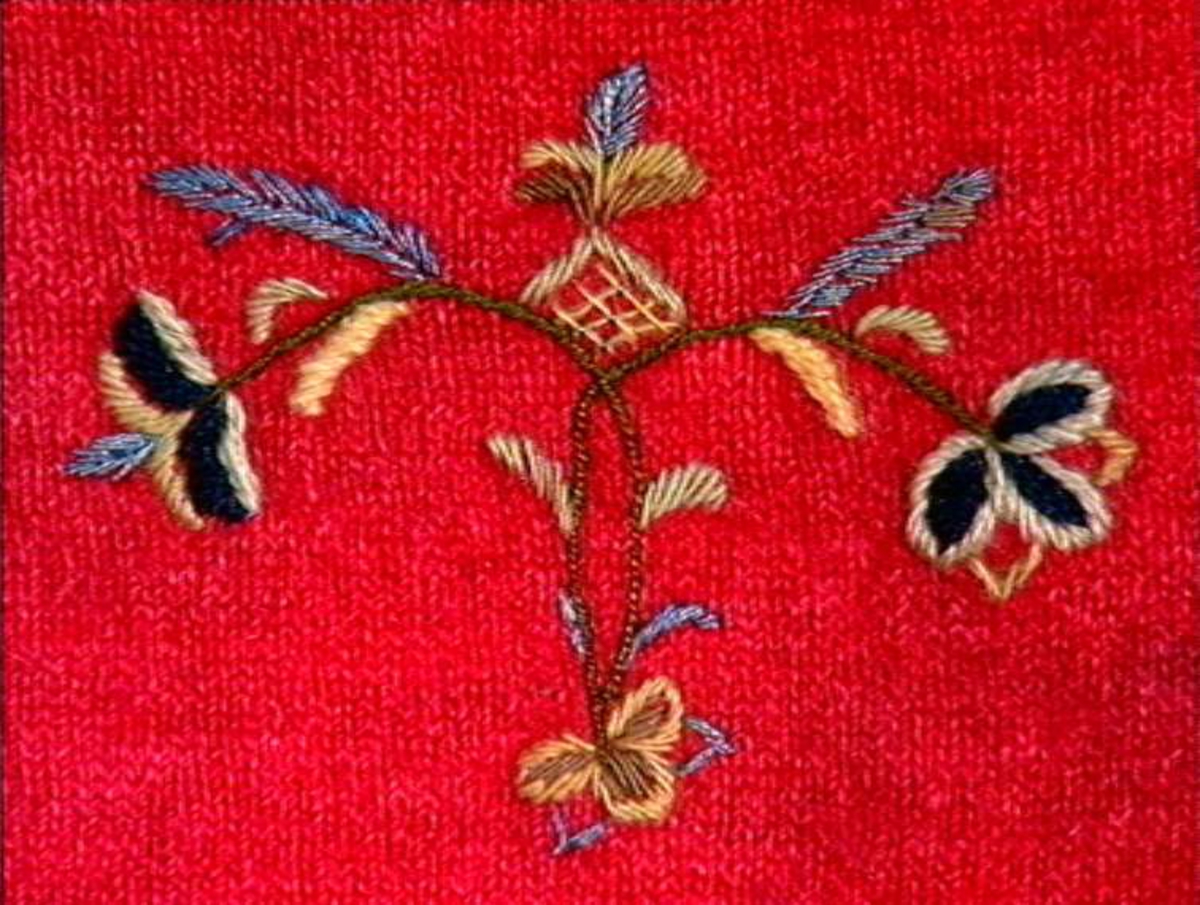 Rød strikket fingervante av ull, dekor av broderi og frynser.