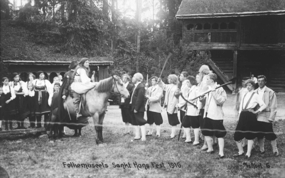 St. Hans fest på Norsk Folkemuseum i 1916. Par på hest foran folkedraktkledde deltakere.