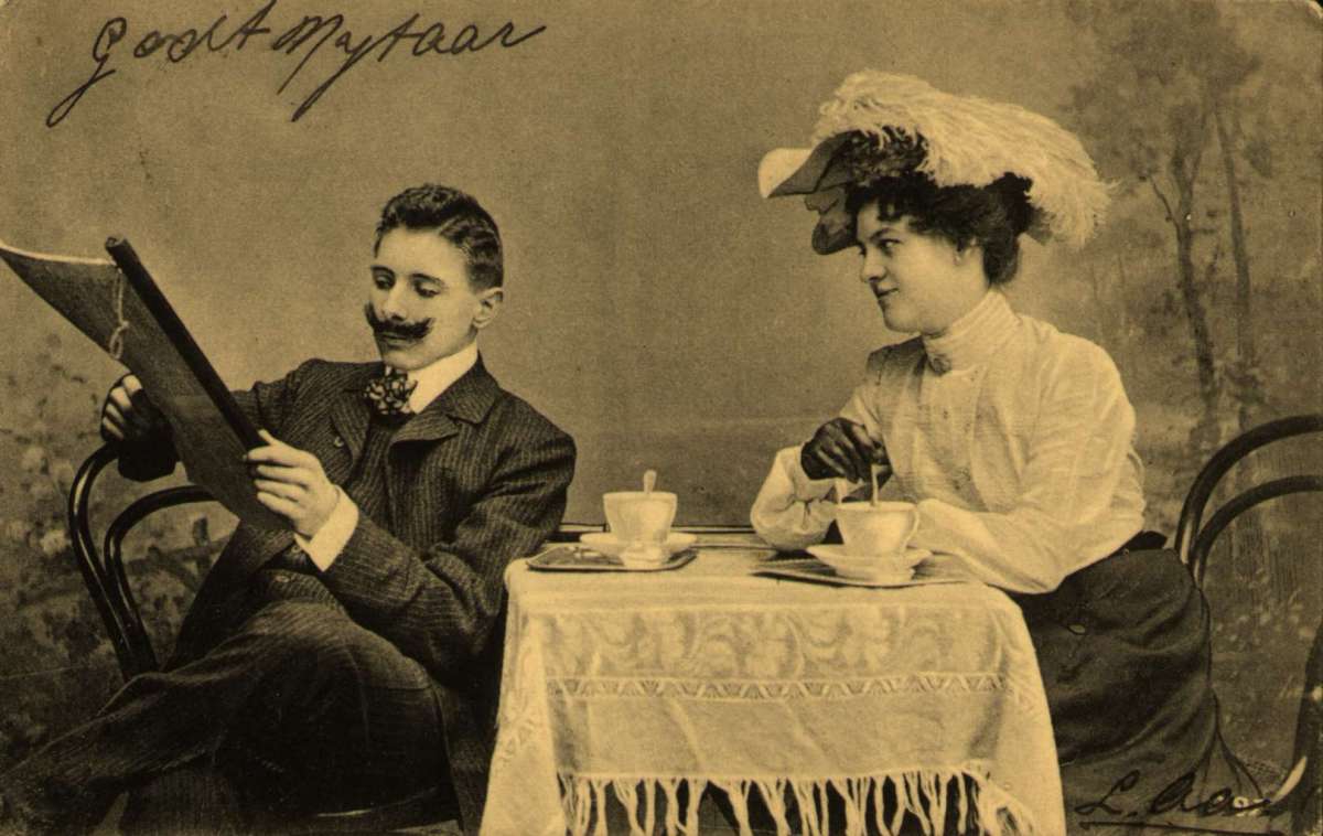 Postkort. Nyttårshilsen. En kvinne og en mann sitter ved et bord og drikker kaffe. Han leser for henne. Stemplet 30.12.1904