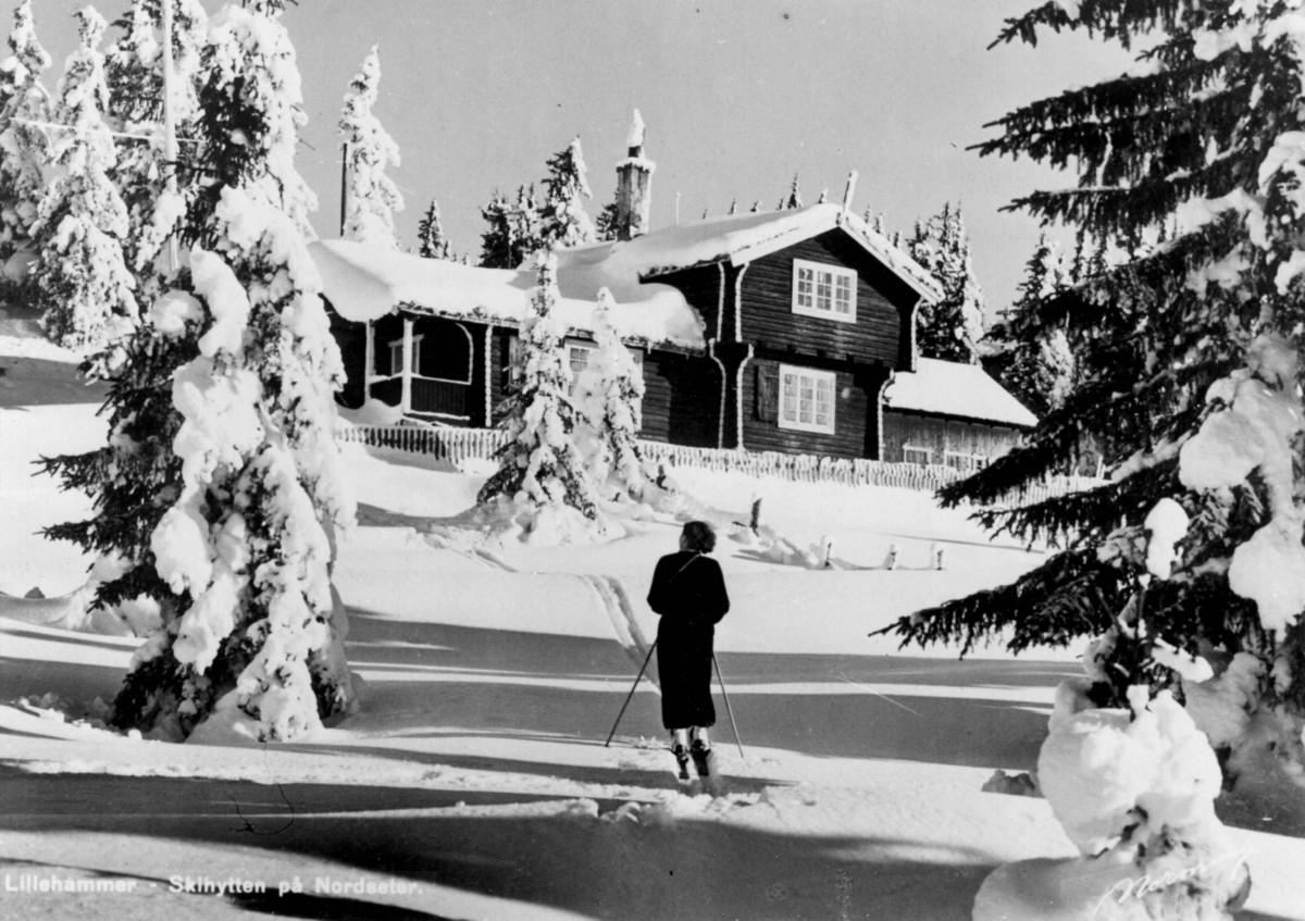Avfotografert postkort. En skiløper foran Skihytten på Nordseter ved Lillehammer.