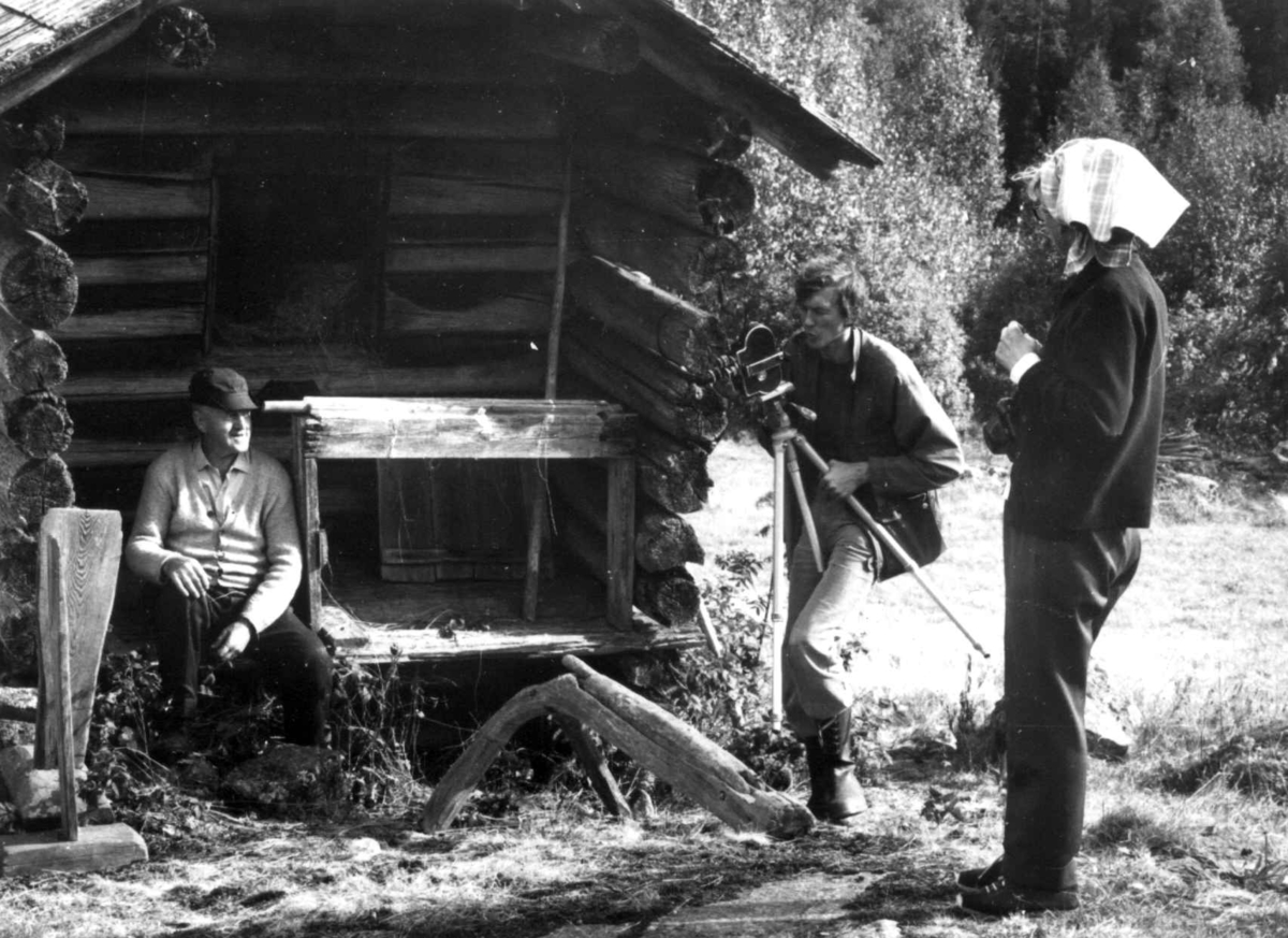 Fotograf Bjørg Disington og konservator Trond Gjerdi under filmopptak på Harstadsetra om linarbeide i september 1975. Olav Askerud sitter foran kjona, med 2 linbråker og en skakestol.