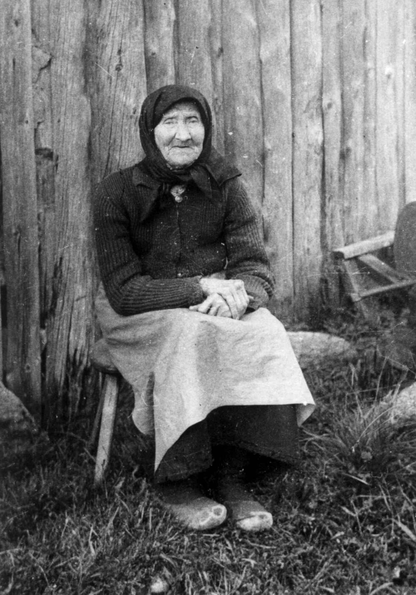 Fru Anna Ånensdatter Grostøl sitter på en stol foran en husvegg. Eiken 1937.