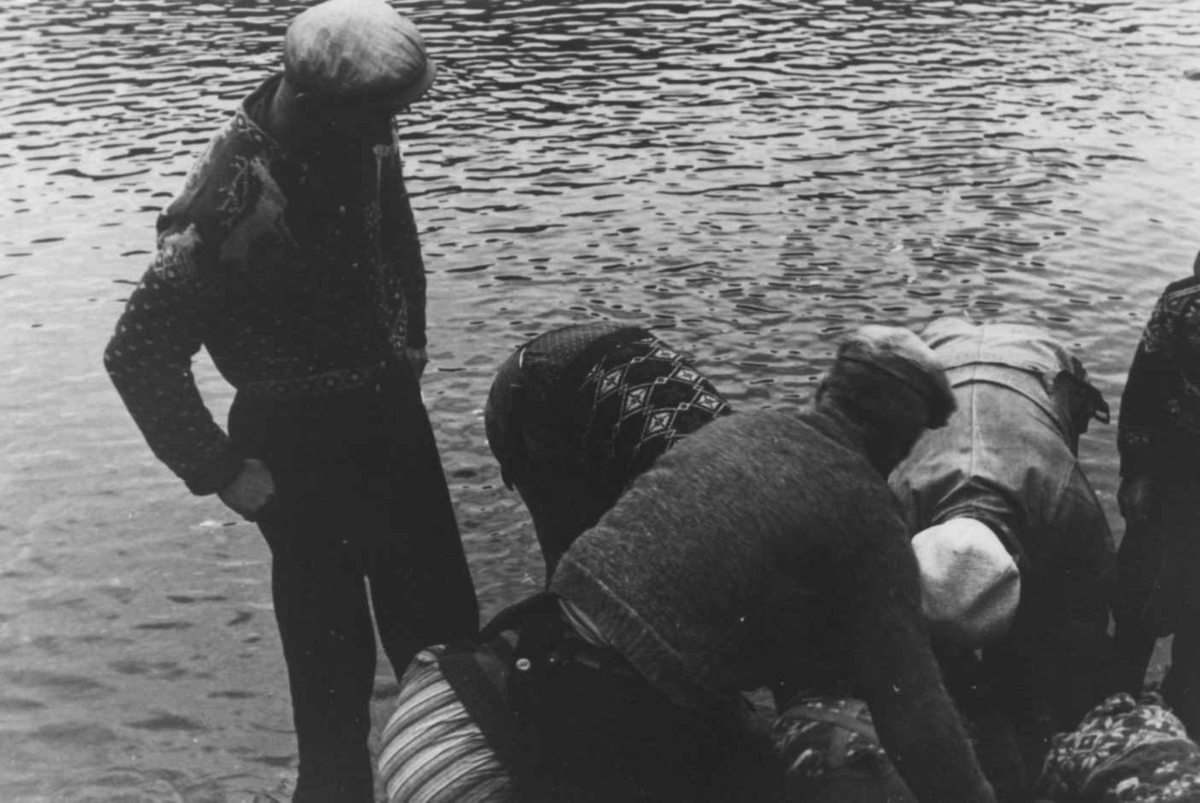Fiske. Nærbilde av en lite gruppe mennesker samlet om et fiskegarn i strandkanten. Åseral, Vest- Agder 1943.