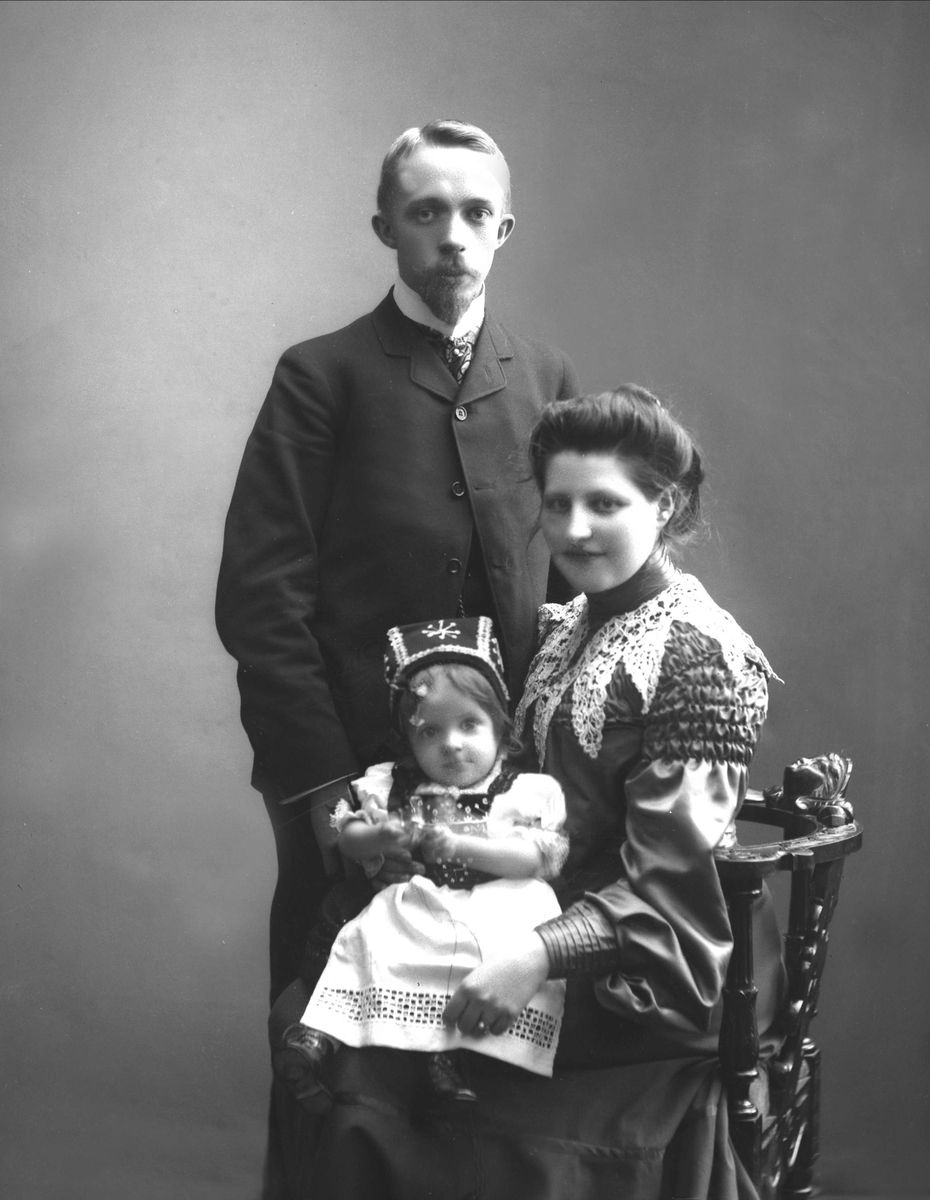 Gruppeportrett, mann står bak stol med kvinne med barn på fanget.