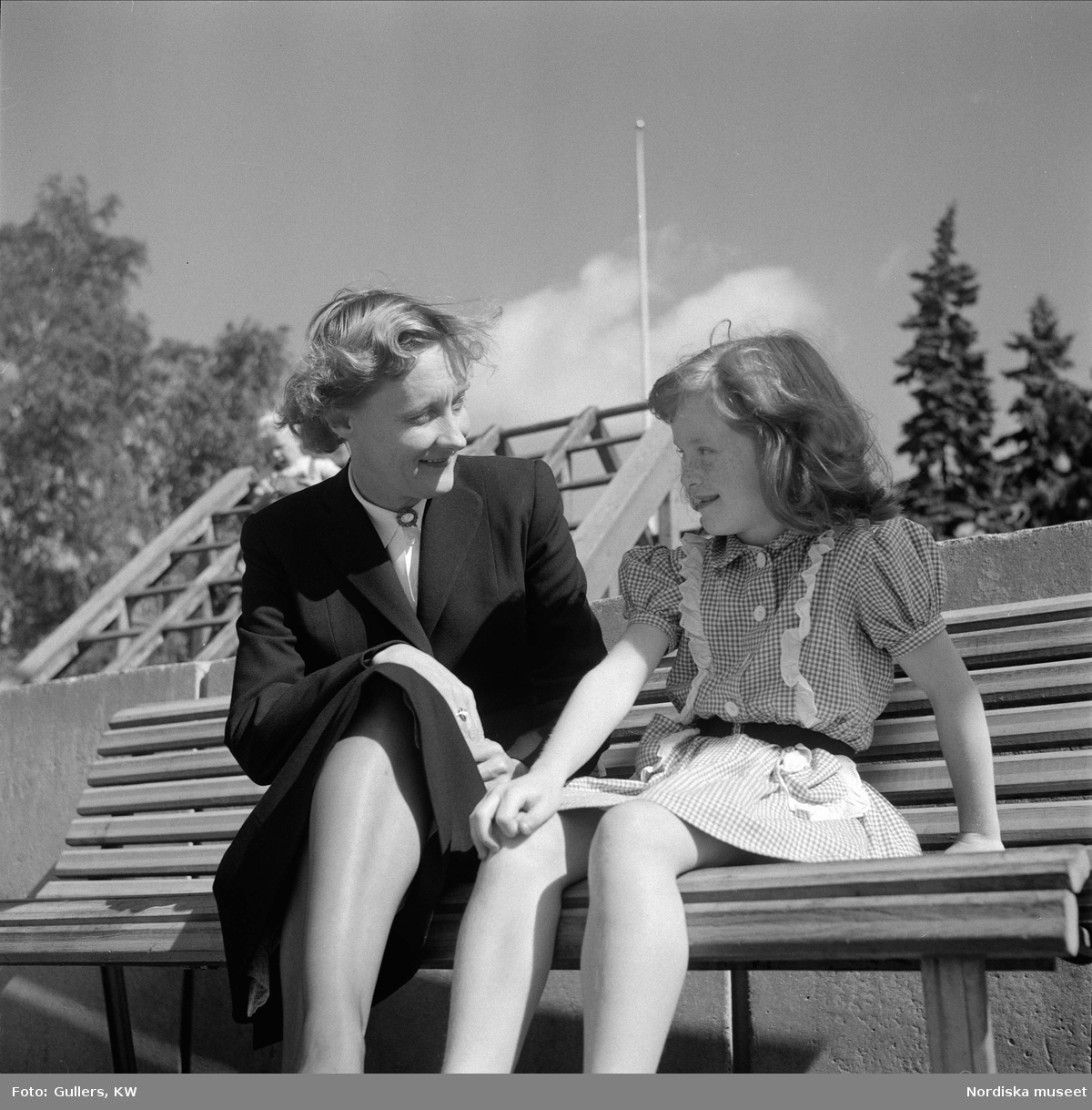 Astrid Lindgren sitter på bänk och pratar med flicka. 