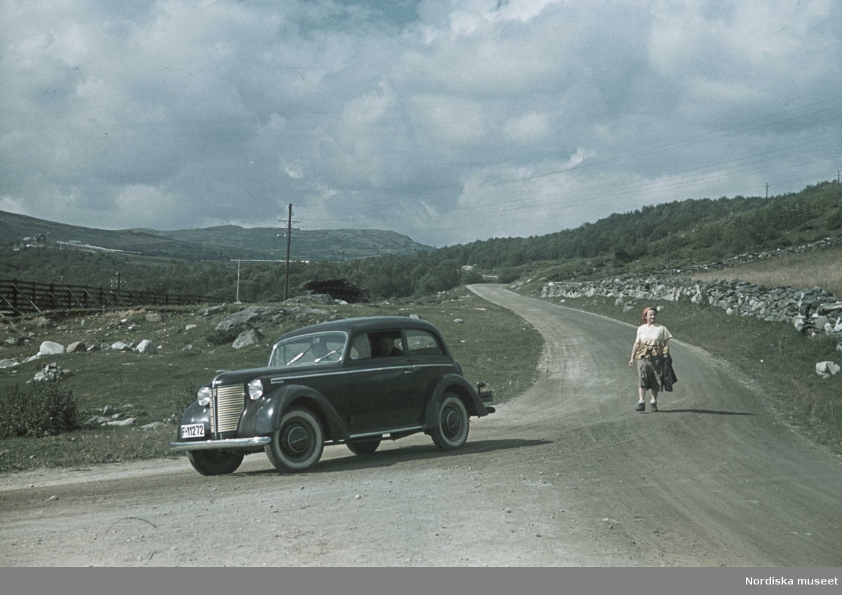 Bil av märket Opel Kadett samt gående kvinna på landsväg.