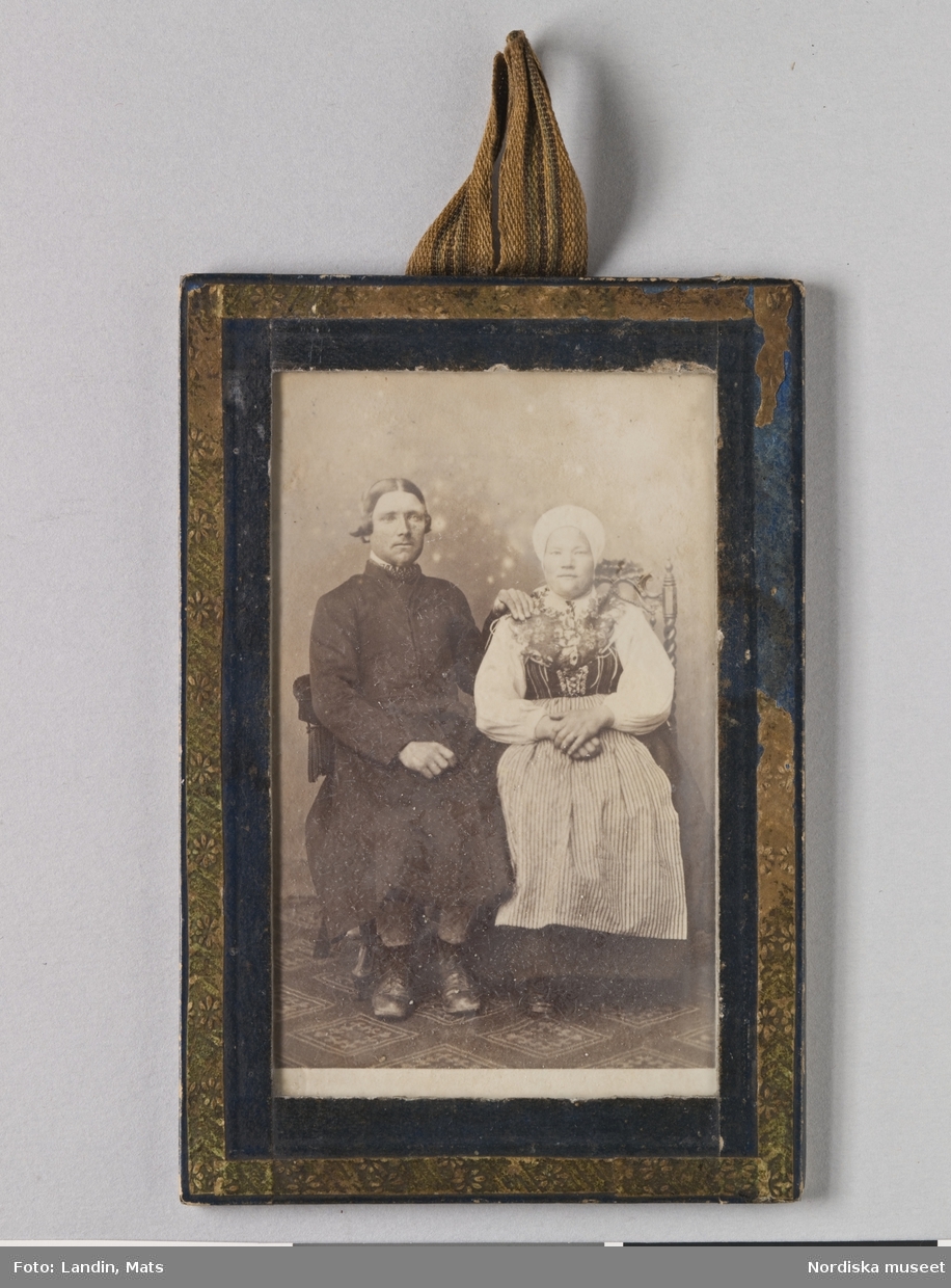 Porträtt, helfigursbild av man och hustru.Föreställer häradsdomare Bröms Olof Larsson, f. 1837, med hustru i hans första gifte, i Leksandsdräkt. Fotografi i visitkortsformat i ram. 
Nordiska museet inv.nr 213230.
